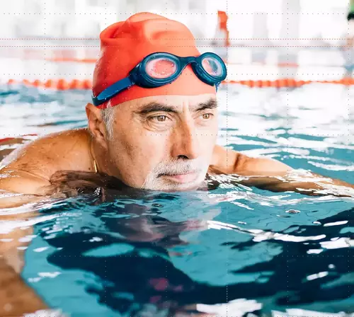 An elderly man in an orange swimming cap at the swimming pool
