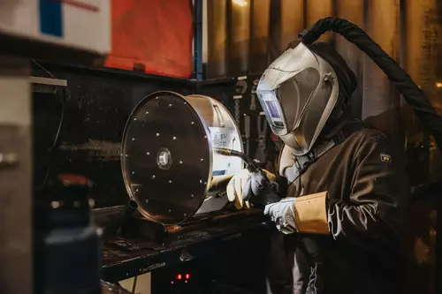 A person in a welding suit welding a metal wheel